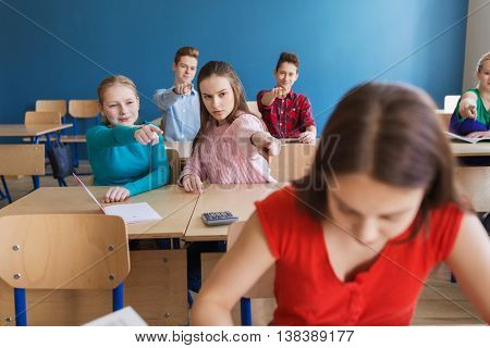 education, bullying, conflict, social relations and people concept - students teasing and judging girl classmate behind her back at school