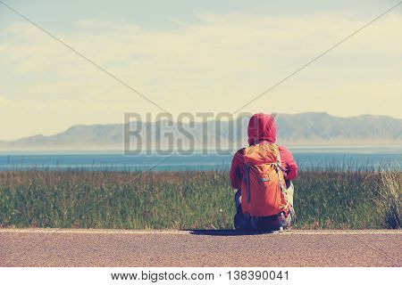 young woman backpacker sit on roadside taking a rest face the beautiful landscape