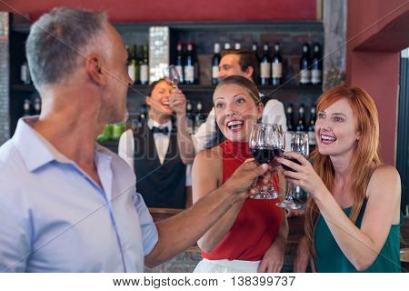 Friends toasting with a glass of red wine at bar counter in a bar