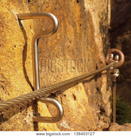 Detail of steel anchor eye and rope end anchored into sandstone rock. Iron twisted rope fixed in block by screws snap hooks.  Trekking via ferrta.