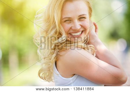 Caucasian smiling girl in white tank top sleeveless. Model glance back. Image with lens flare effect