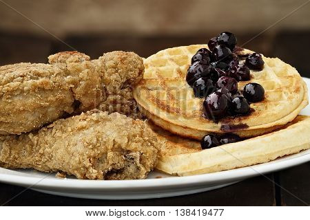 Three pieces of deep fried chicken with waffles served with fresh blueberry sauce. Extreme shallow depth of field.
