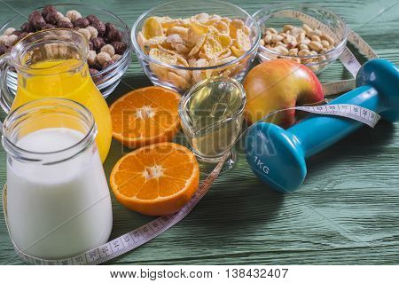 The concept of a healthy lifestyle. Cornflakes orange juice yogurt nuts honey tangerines apple dumbbell and measuring tape on rustic wooden table. Cereals and fruit - diet and breakfast