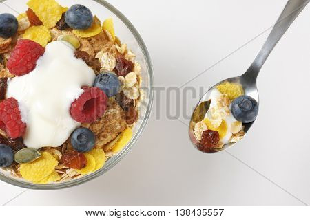 bowl and spoon of cereals with berry fruit and white yogurt on off-white background with shadows