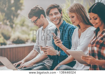 Technologies making lives easier. Group of young people holding different digital devices while man looking at camera and holding mobile phone