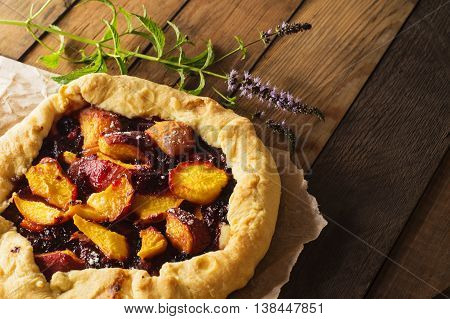Homemade flan with plums and peaches. Delicious galette with fruits on rustic wooden background.