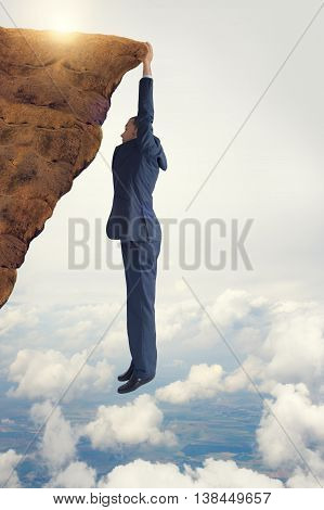 business concept challenge businessman clinging on to a cliff edge