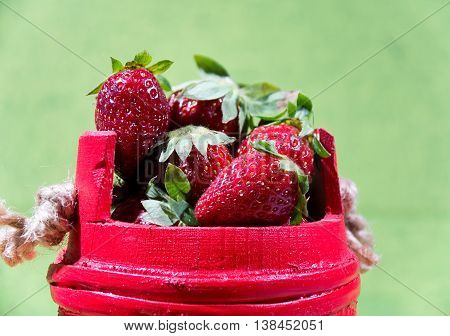 Red basket full of strawberries on green background