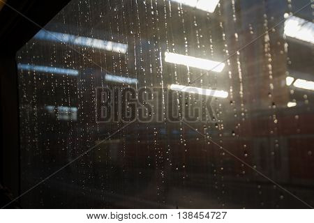 Sunrise through Raindrops on Window of Train in Station
