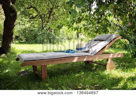 garden daybed made of wood with a summer hat on a sunny meadow in the orchard, enjoy leisure