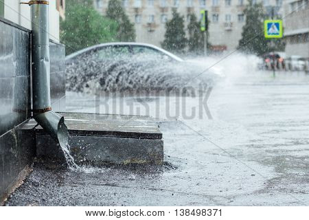 Rain water flowing from metal drainpipe during a flood. splashes of cars background. concept of protection against heavy downpours