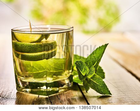 Alcohol drink. On wooden boards is glass with alcohol green transparent drink. Drink number hundred fifty three mohito cocktail with lime. Country outdoor. Light background.