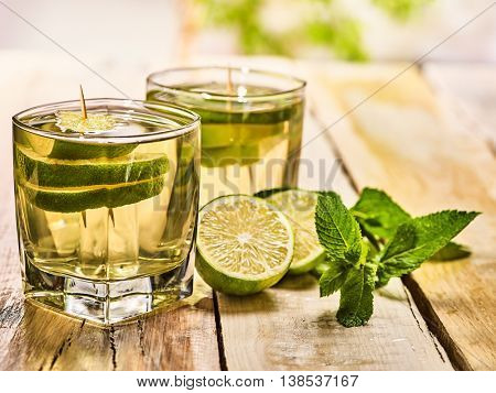 Alcohol drink. On wooden boards two glasses with alcohol green transparent drink. A drink number hundred sixty five mojito cocktail with half lime and mint . Country life style. Light background.