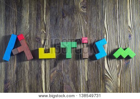 Word Autism built of wooden puzzles on a wooden background. Concept of autism word.