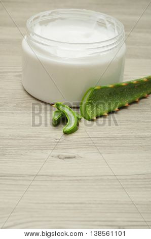 White beauty cream in a jar displayed with aloe Vera on a wooden background