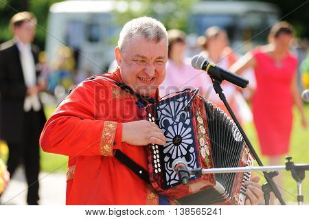 Orel Russia - July 08 2016: Russian Valentine Day - Petr and Fevronia. Senior man in red outfit playing garmoshka Russian accordion closeup