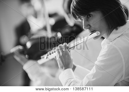 Professional female flustist playing her instrument on stage with classical music symphony orchestra