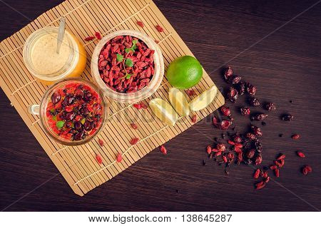 Fresh antioxidant herbal tea from dried goji berries, sweetbrier and blueberry in a glass cup on wooden background with lime and honey. Alternative medicine. Recovery.Rejuvenation. Slimming. Top view.