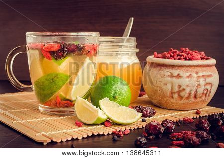 Fresh antioxidant herbal tea from dried goji berries, sweetbrier and blueberry in a glass cup on wooden background with lime and honey. Healthy food. Alternative medicine. Recovery. Slimming.