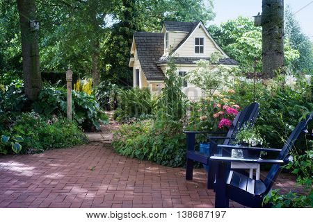A charming playhouse is seen beyond two wooden chairs in a shaded garden patio.