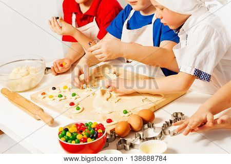 Kids in white aprons making candy filled cookies with cookie cutters on wooden desk