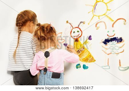 Two little painters, preschool girls drawing funny picture at the wall, isolated on white