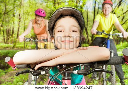 Portrait of happy smiling girl in bicycle helmet, bracing against handlebar of the bike