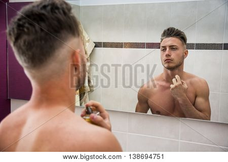 Handsome shirtless young man in his home bathroom, spraying cologne or perfume on neck