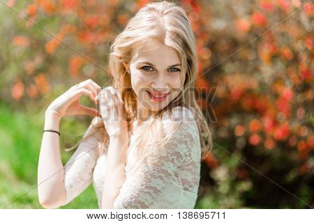 Beautiful blonde showing heart shape. Bloomig garden. Good weather