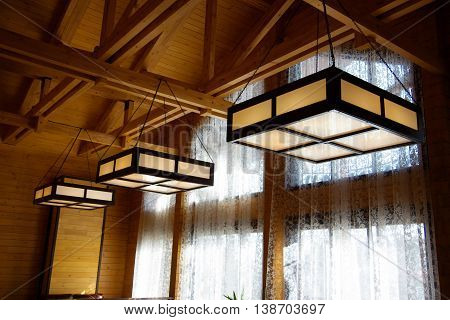 Large glass and wooden chandeliers hanging under the wooden ceiling by chains.