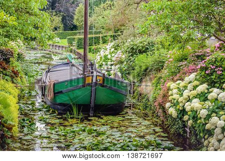 Historic restored ship in the narrow canal of the small Dutch village of Drimmelen. It's summer and many shrubs and plants are in full bloom.