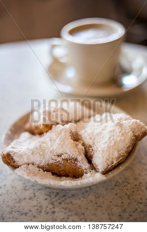 Beignets (French style donuts) topped with sugar and a cup of coffee in the background
