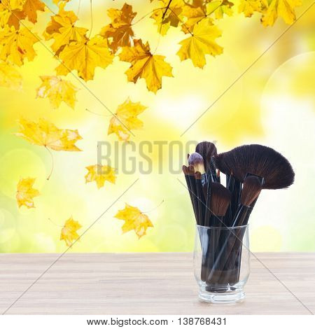 set of black brushes, lipsticks, maskara and eye shadows, fall park in background