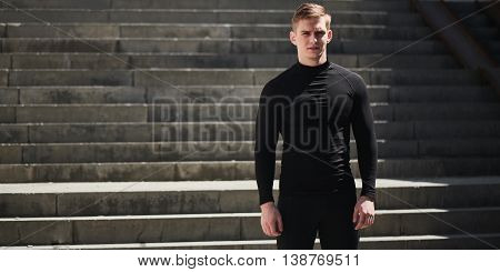 Portrait of a athletic man in a black slinky dress against the backdrop of the stairs