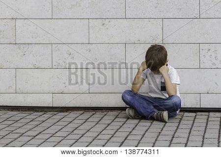Sad, lonely, unhappy, disappointed, upsed, tired child sitting alone on the ground Outdoor