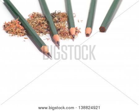 five sharpened and unsharpened green pencils with pencil sawdust