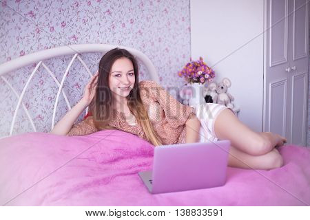 woman in pink room sitting on the bed and playing or watching cartoons price. Girl sitting at home uses advanced fashion technology