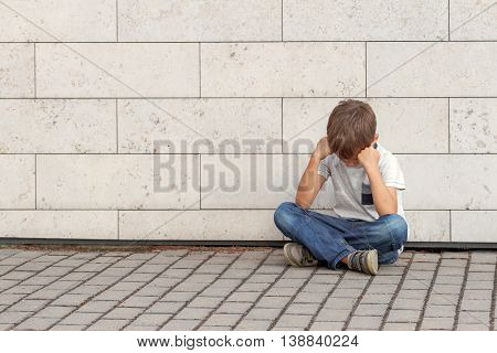 Sad, lonely, unhappy, upsed, disappointed tired child sitting alone on the ground Outdoor