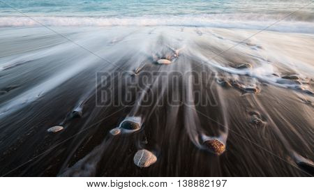 Pebbles in the beach on a black sand and flowing sea water creating nice textures. Long exposure image.