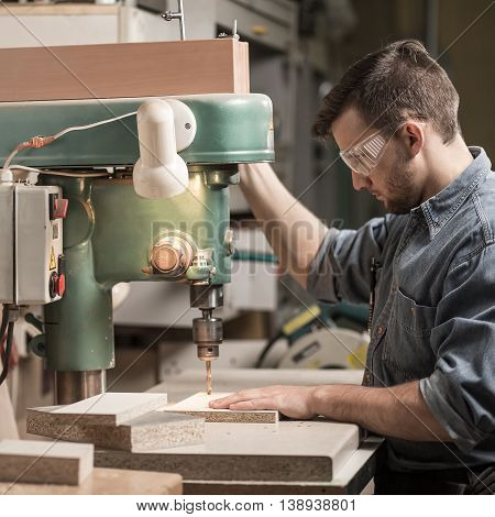Young carpenter working at wood manufacture in glasses