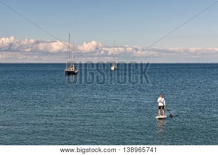 Swanage Dorset UK - July 2016. Eldery male paddles a paddleboard at the sea