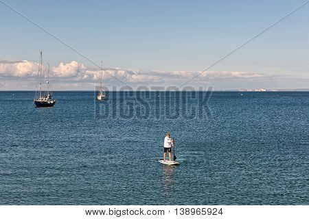 Swanage Dorset UK - July 2016. Eldery male paddles a paddleboard at the sea