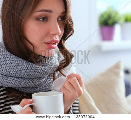 Portrait of a sick woman blowing her nose while sitting on the sofa.