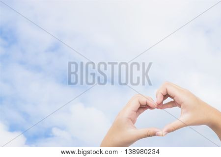 kid hands making a heart shape with blue sky background