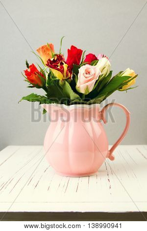 Rose flowers in pink jug on wooden table