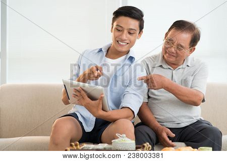 Senior Man And His Grandson Watching Something On Tablet Computer