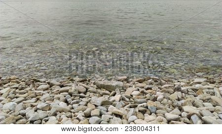 The Beach With Colorful Pebbles And A Bustling Ocean. Background