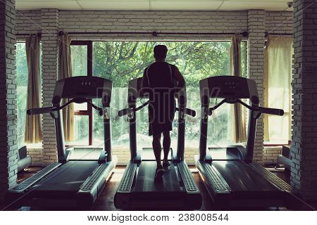Rear View Of Sportsman Running On Threadmill In Small Local Gym