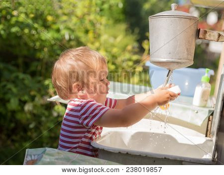 Small Boy, Toddler, 2 Years Old, Blonde, In Striped T-shirt Washes His Hands Under Washstand Outdoor