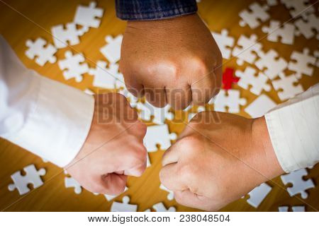 The Hands Of Three Business People Have A Jigsaw Puzzle As A Background.
